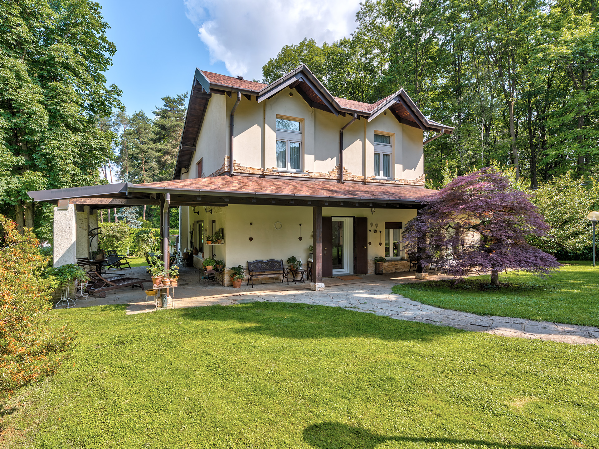 Two-story beige house with a brown roof, covered patio, stone walkway, and a large purple Japanese maple tree in the yard. [AI-generated text]