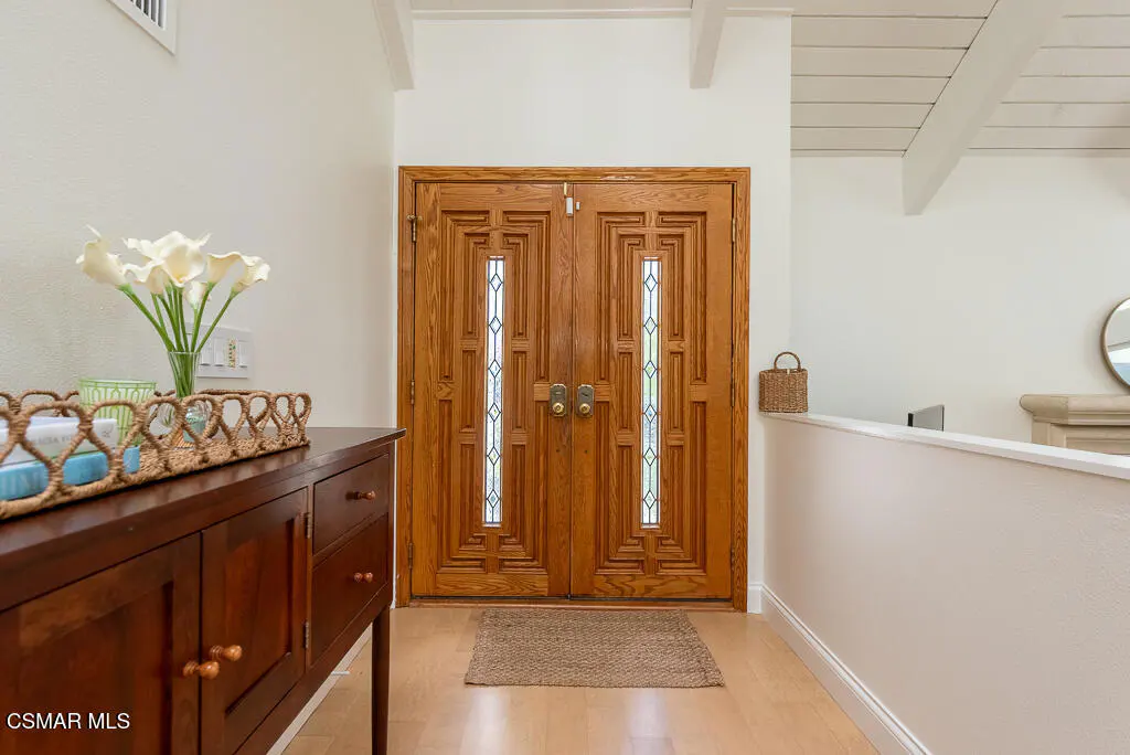 Entryway with a dark wood console table, white calla lilies, and a carved wood double door with glass panels.