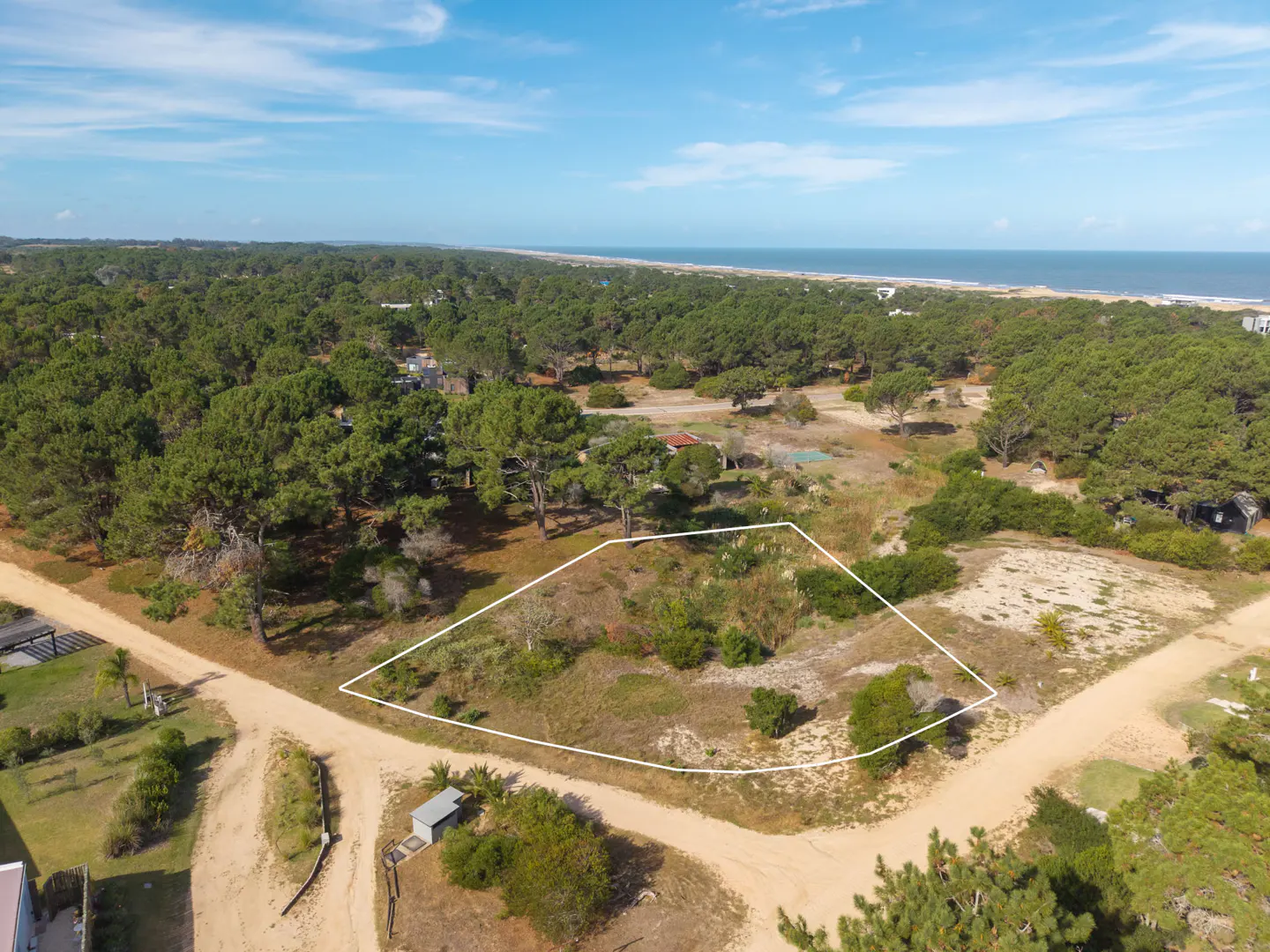 Aerial view of a vacant lot outlined in white, surrounded by trees, with the ocean visible in the background.