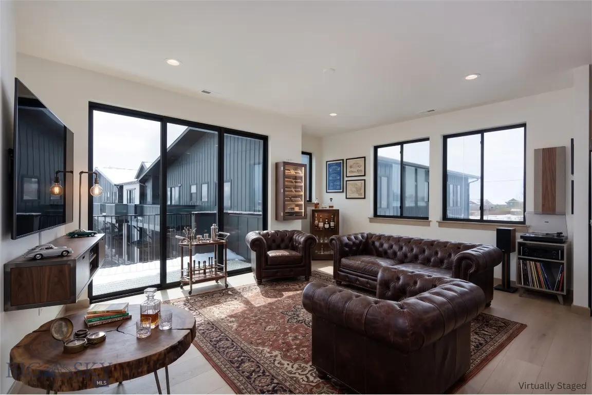 Living room with brown leather sofas, wood table, bar cart, and large windows overlooking snowy rooftops.