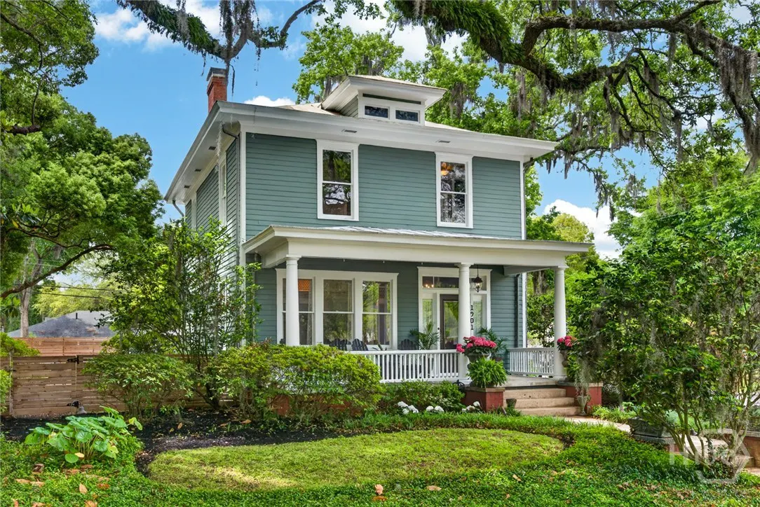 Two-story teal house with white trim and a front porch, surrounded by lush green trees and lawn.