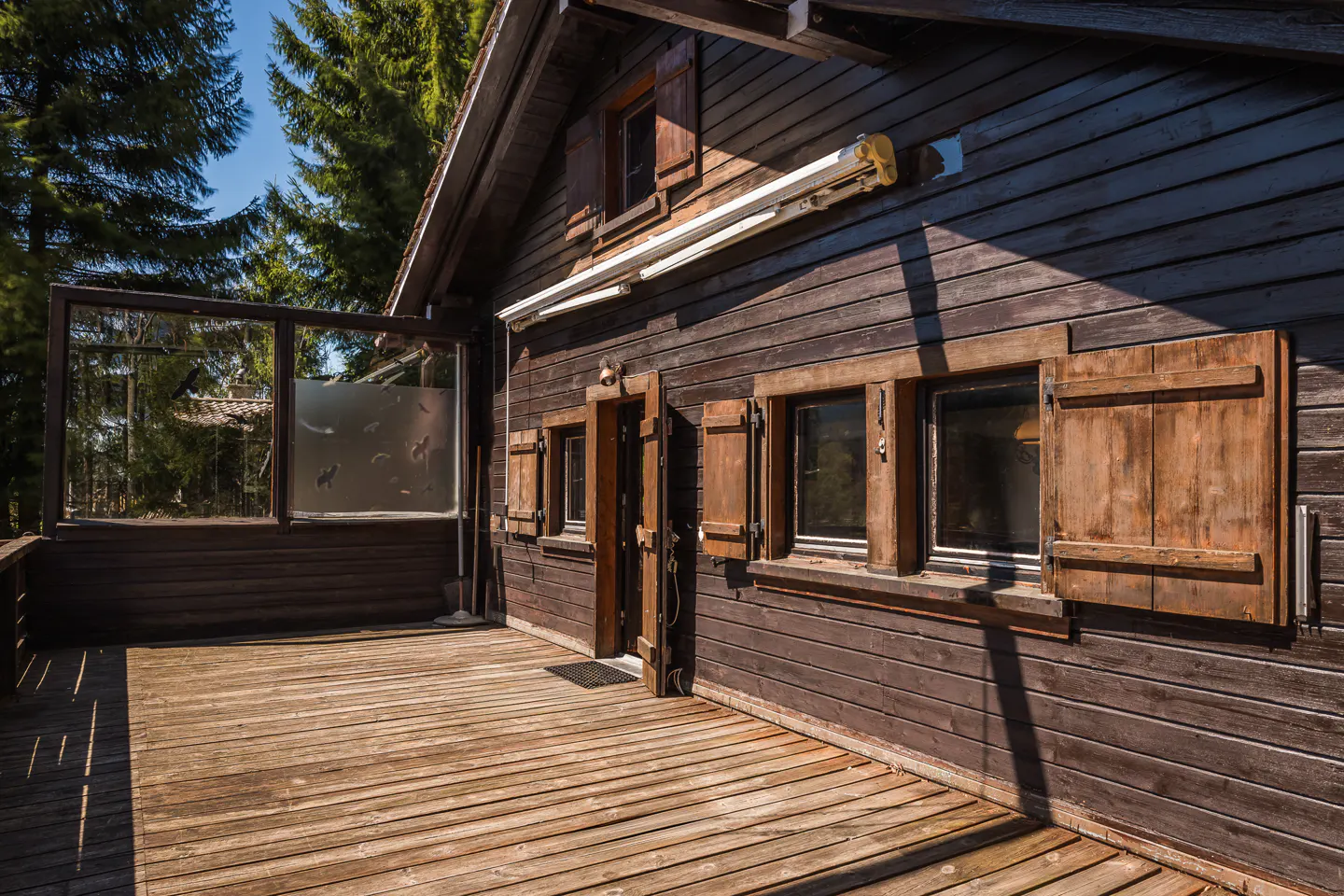 Exterior view of a brown wooden cabin with a deck, open door, and window shutters.