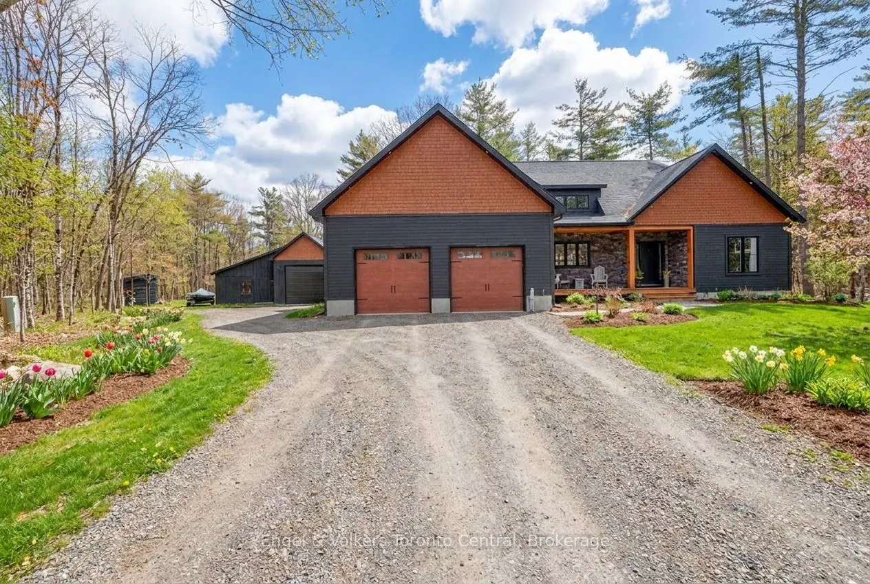 Exterior view of a modern, dark gray house with a brown roof and garage doors, surrounded by green lawns and trees.