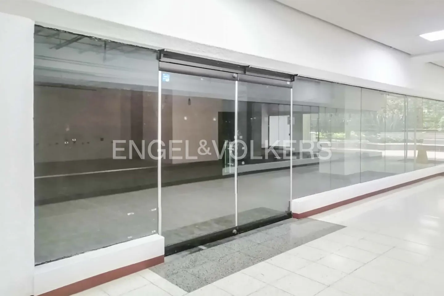 Engel & Volkers storefront with glass sliding doors and windows in a mall. The interior is empty.