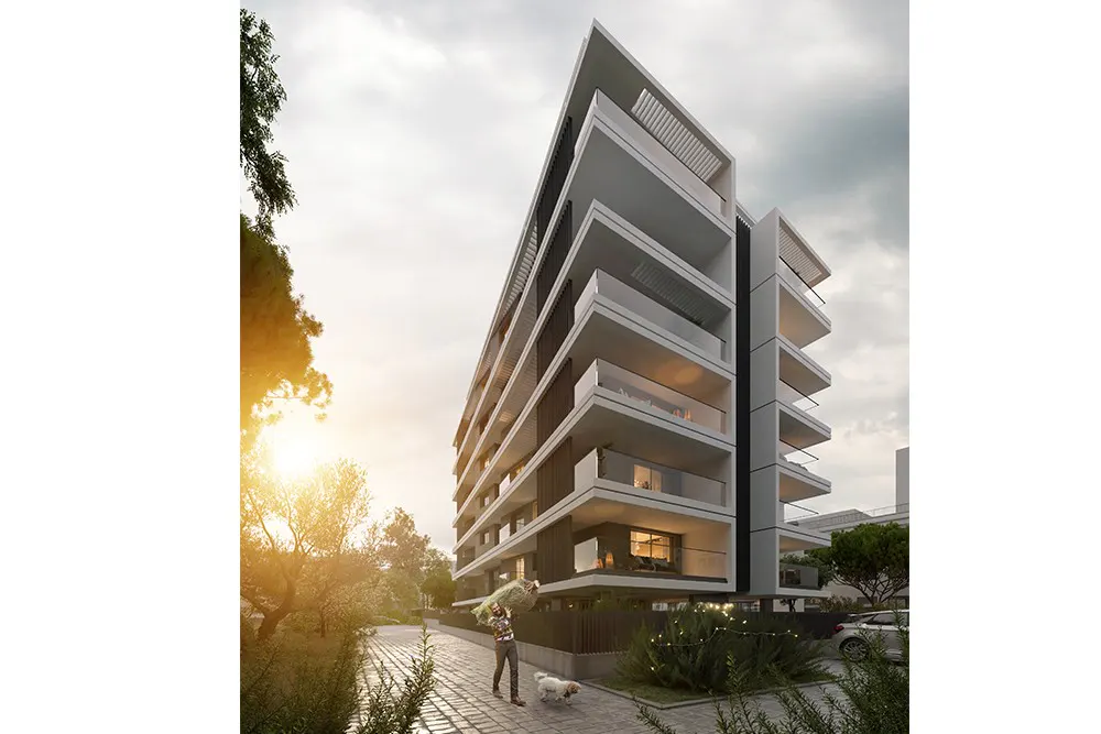 Modern white apartment building with balconies, set against a cloudy sky. A man walks a dog on a paved path in front.