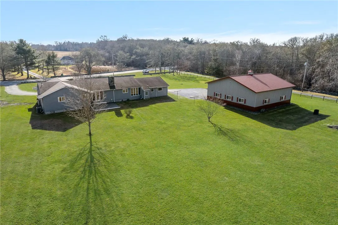 Aerial view of a gray house and barn with a red roof on a large green lawn.