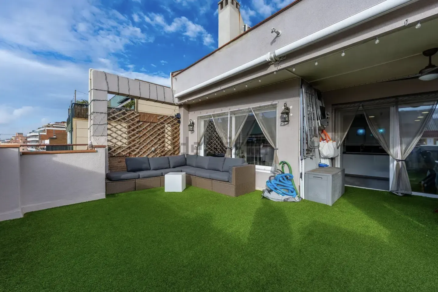 Outdoor patio with green turf, a gray sectional sofa, and a white cube table. The patio has a partial view of the city.
