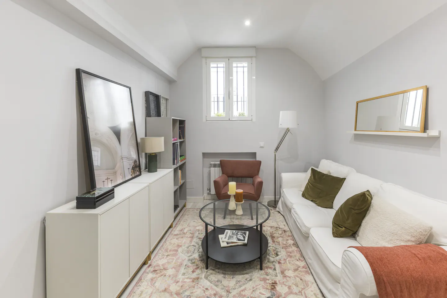Cozy living room with a white sofa, glass coffee table, terracotta armchair, and a patterned rug under a vaulted ceiling.