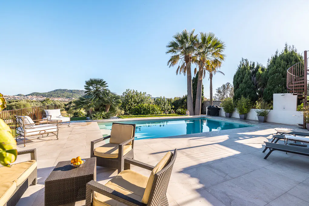 Outdoor patio with a pool, lounge chairs, and palm trees under a clear blue sky.