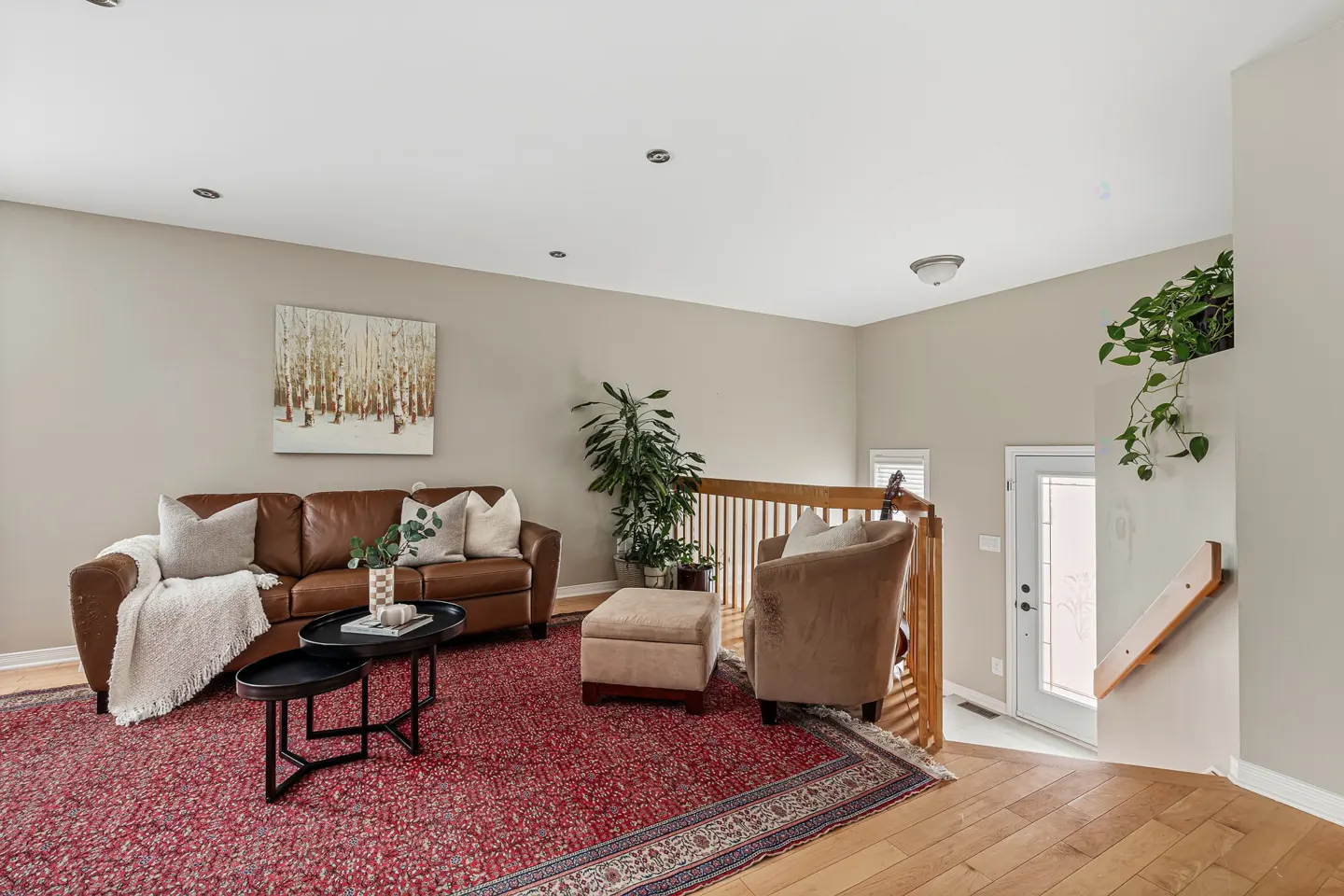 Living room with brown leather sofa, red patterned rug, coffee tables, armchair, and a staircase leading to a front door.