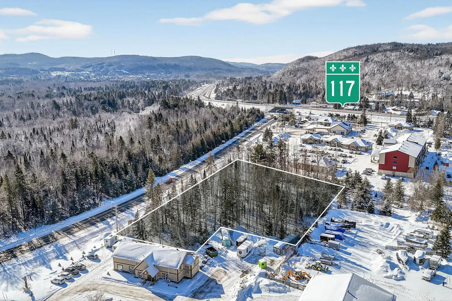 Aerial view of a snow-covered lot outlined in white, near Highway 117, with mountains and trees in the background.