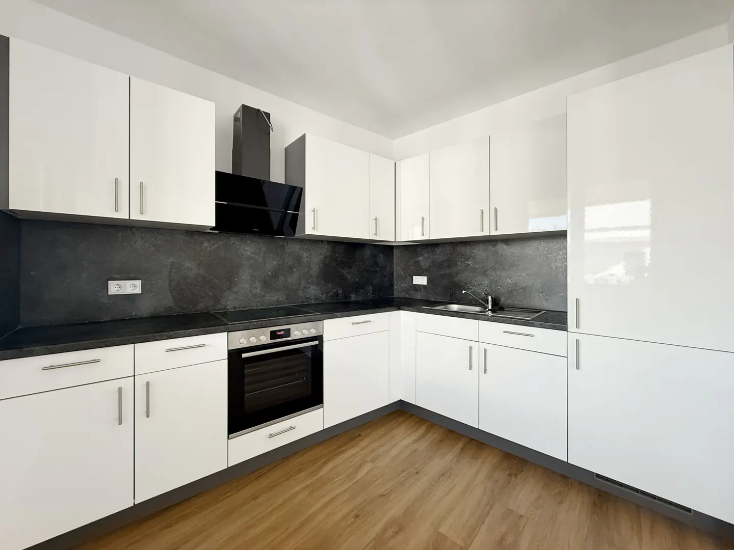 Bright kitchen with white cabinets, black countertops and backsplash, stainless steel sink, and wood-look flooring.