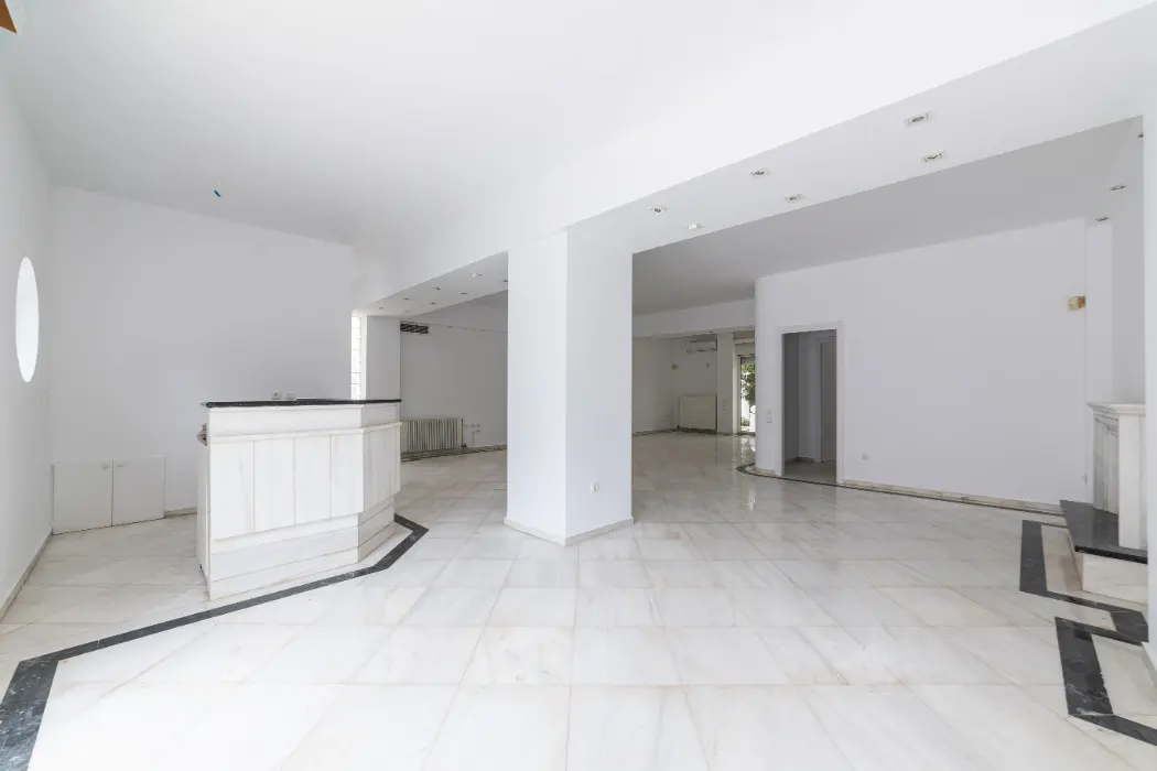 Bright, empty room with white walls, marble floors, and a reception desk. Columns support the ceiling. Black trim accents the floor.