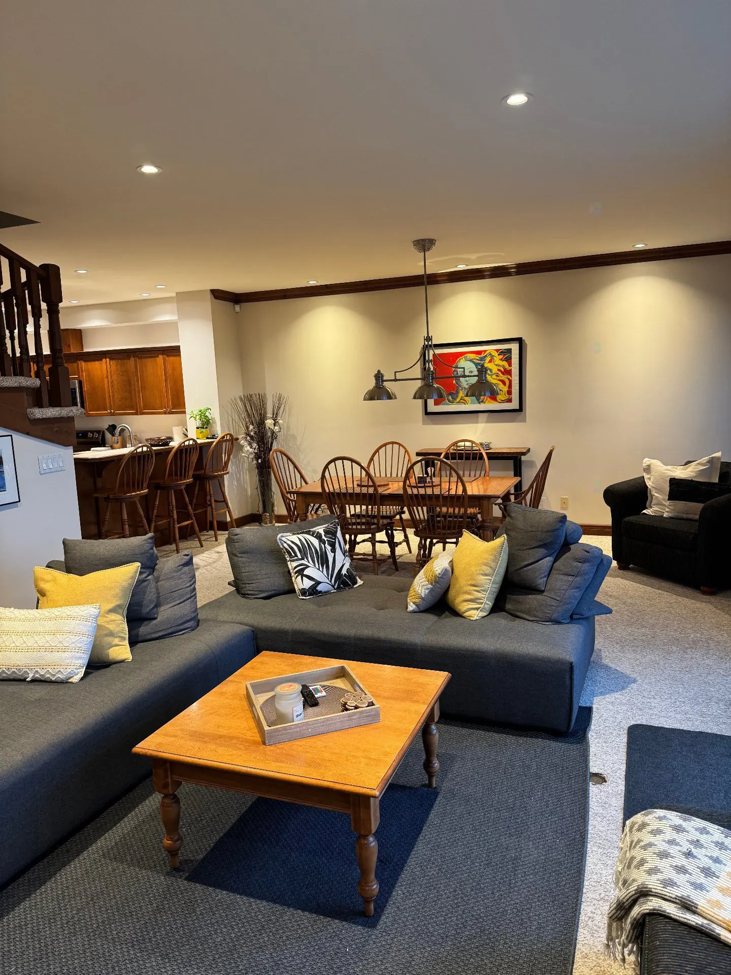 Open-concept living space with a gray sectional sofa, wood coffee table, dining set, and kitchen barstools.