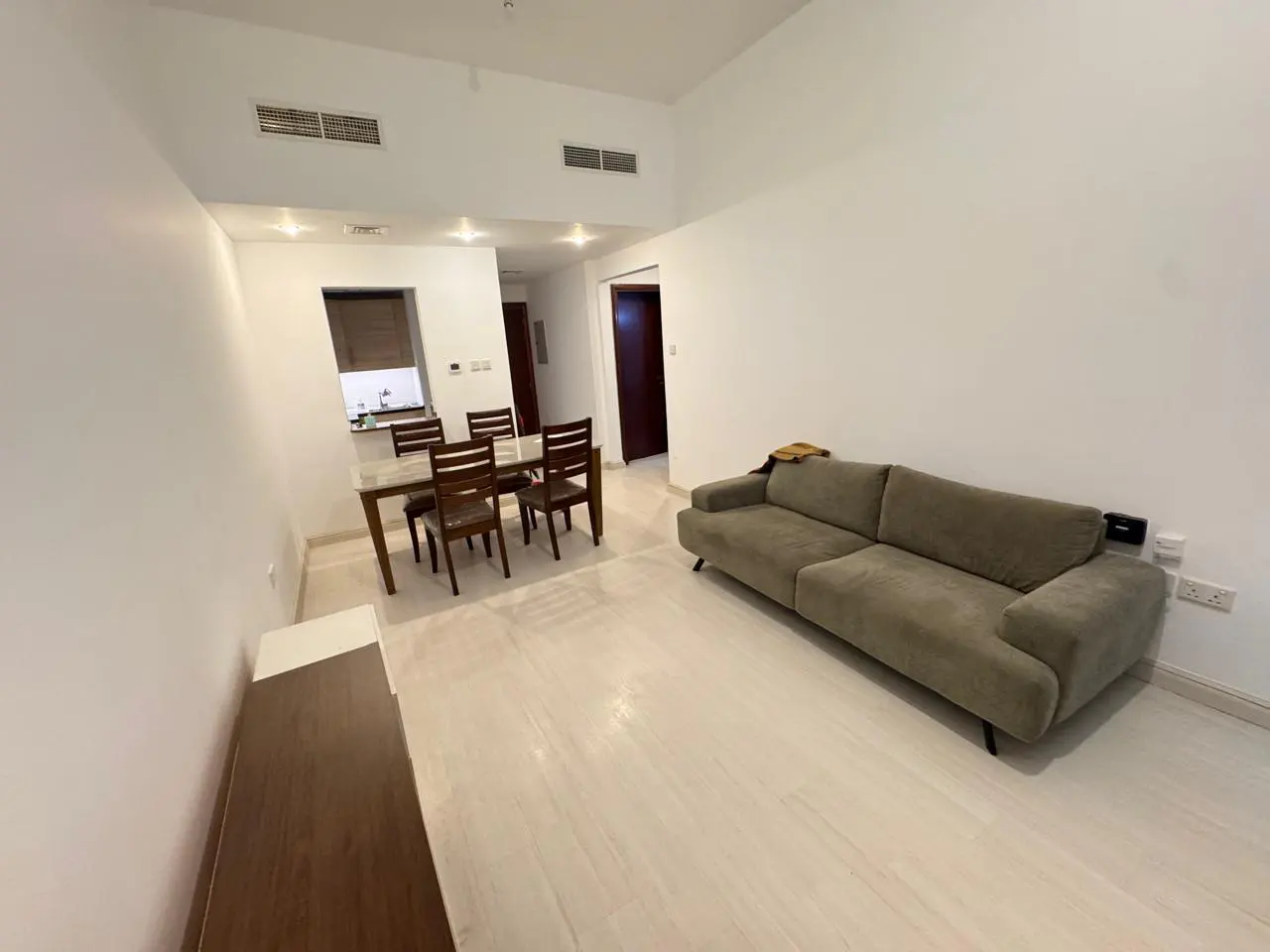 A bright, modern living room with a gray sofa, dining table with chairs, and white walls.
