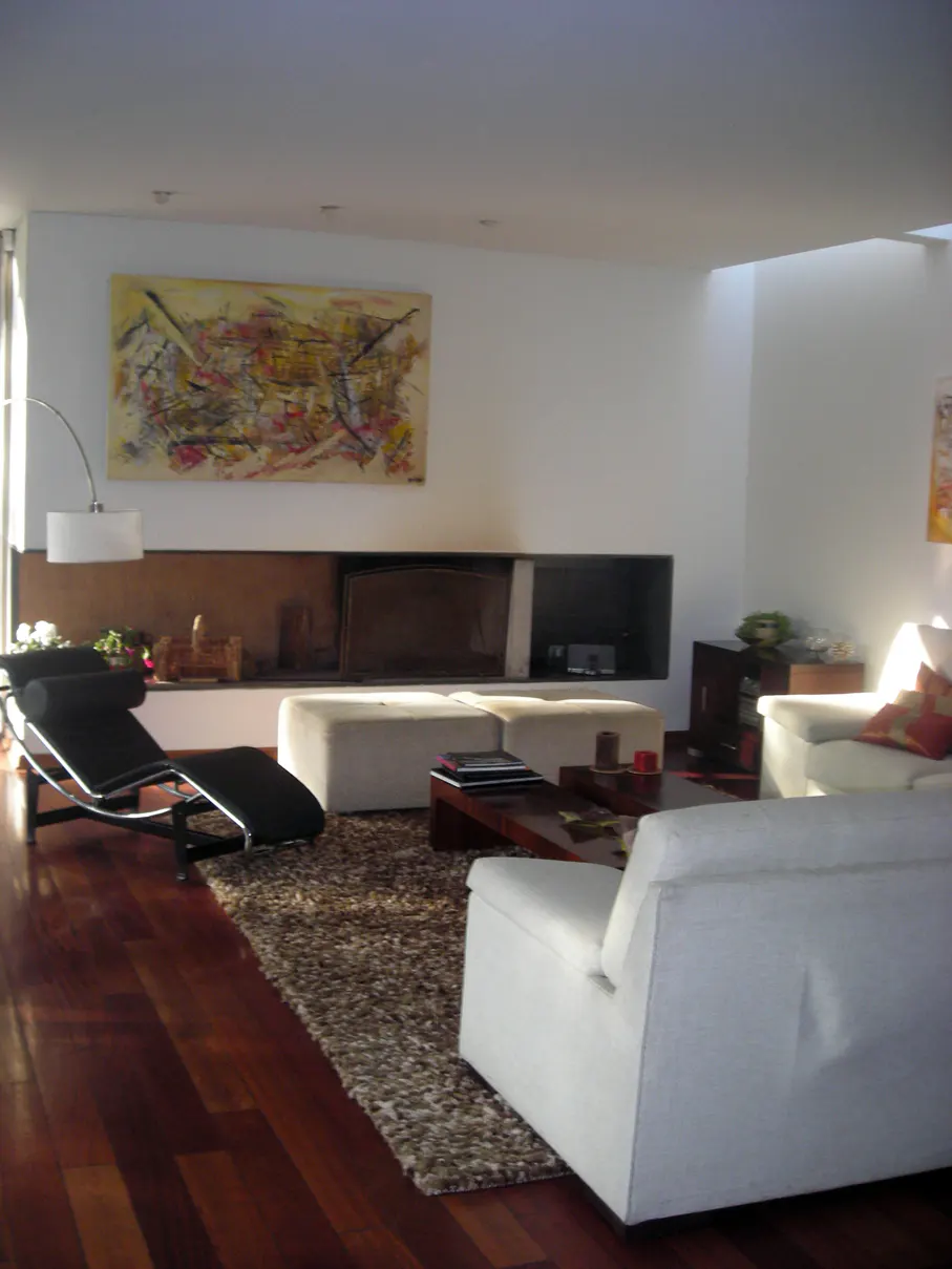 Bright living room with hardwood floors, white sofas, and a black chaise lounge. An abstract painting hangs above a modern fireplace.