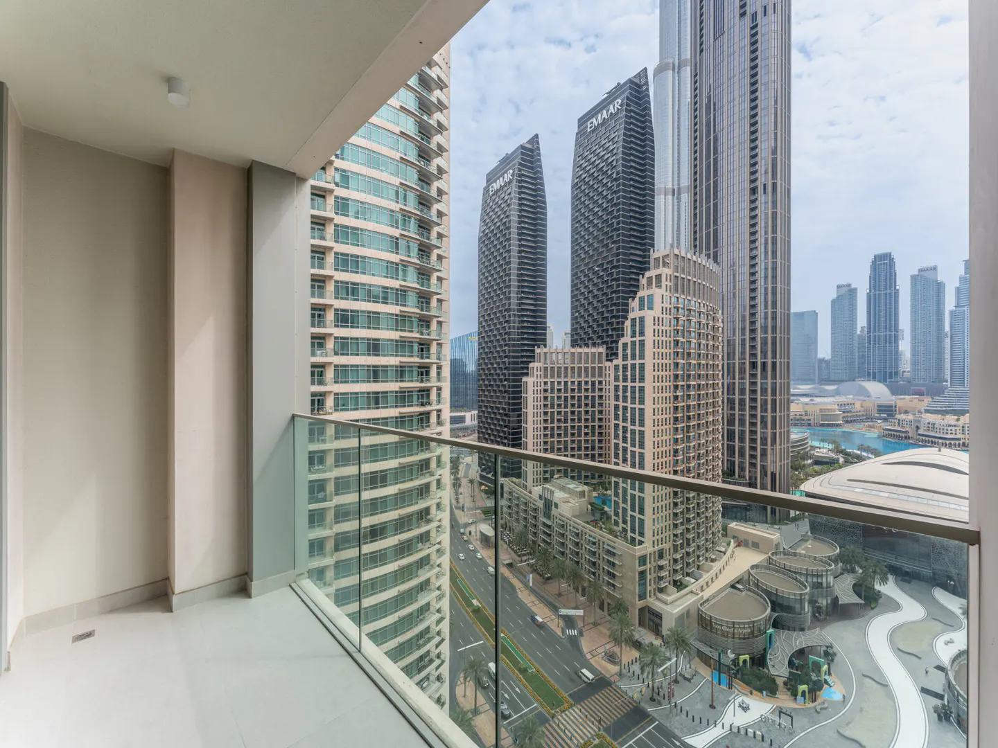 View from a balcony with glass railings overlooking Dubai skyscrapers and a busy street below.
