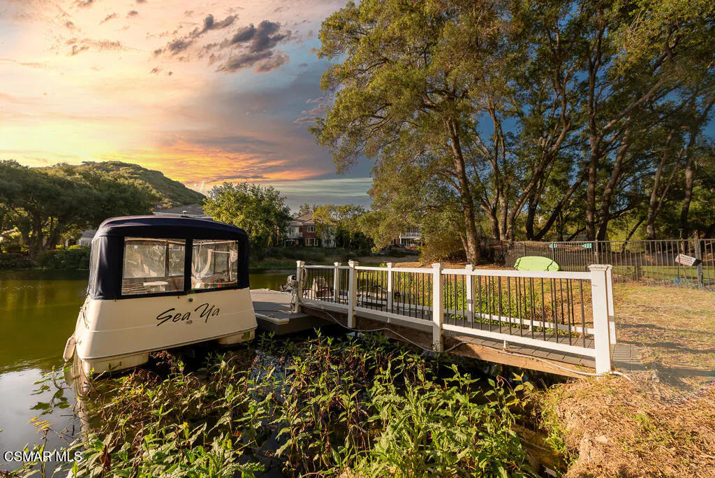 A boat named "Sea Ya" is docked at a white pier on a river with trees and a sunset in the background.