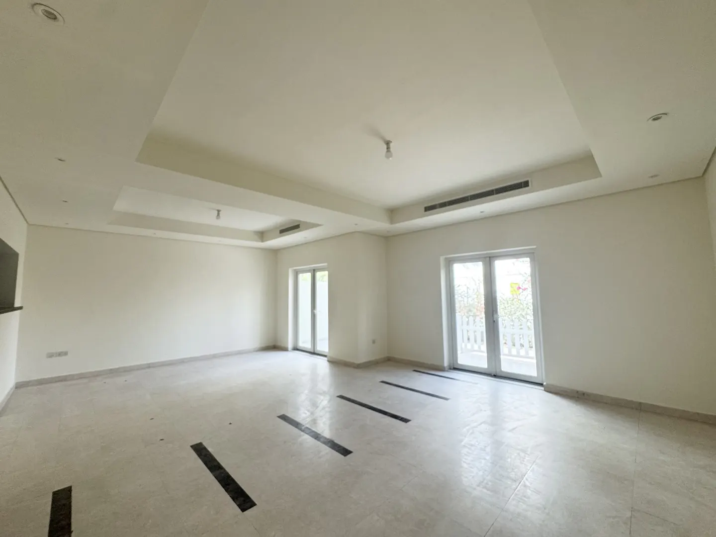 Bright, empty room with white walls, marble floor with black accents, and two sets of white patio doors.