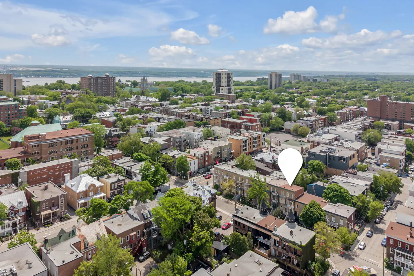 Aerial view of a dense city neighborhood with a white location pin marking a specific brick building under a blue sky.