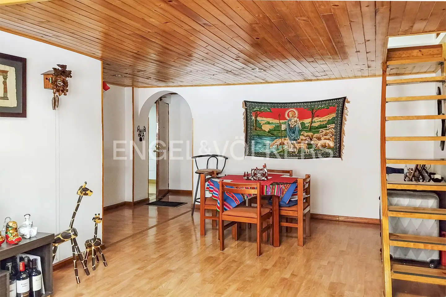 A bright living room with wood floors, a wood ceiling, a dining table, and a wooden ladder to the right.