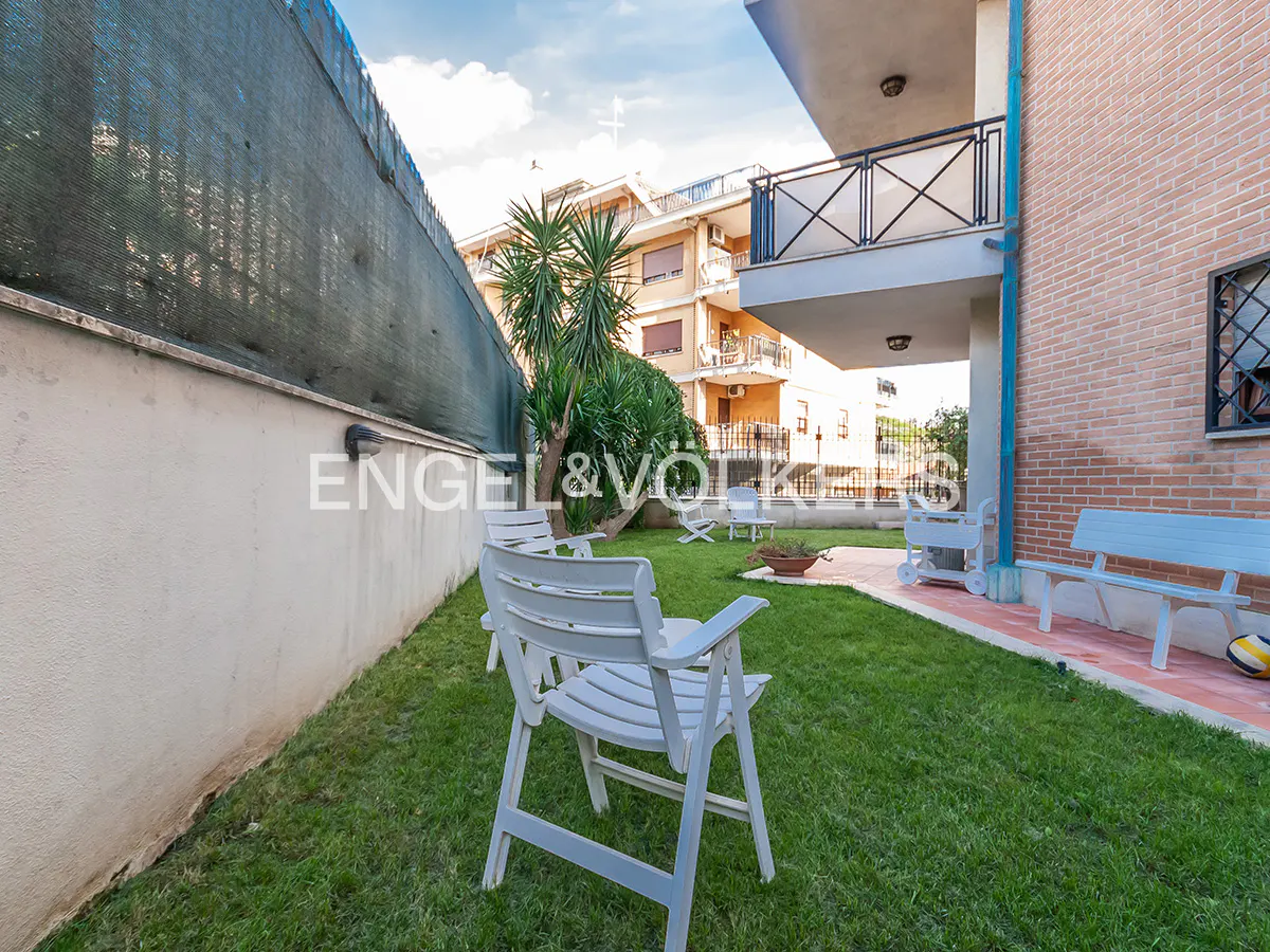 A backyard with green grass, white chairs, and a brick building. The sky is blue with white clouds.