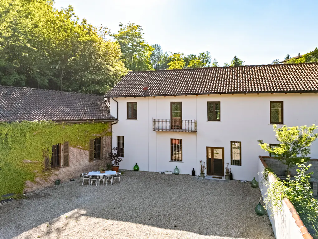 Exterior view of a white two-story house with a brown tile roof and a gravel courtyard with a table and chairs.