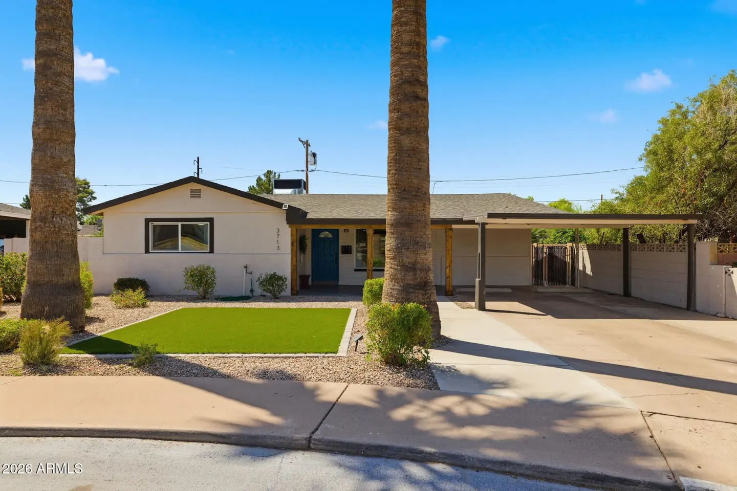 A single-story home with a blue door, green lawn, and a carport on a sunny day.