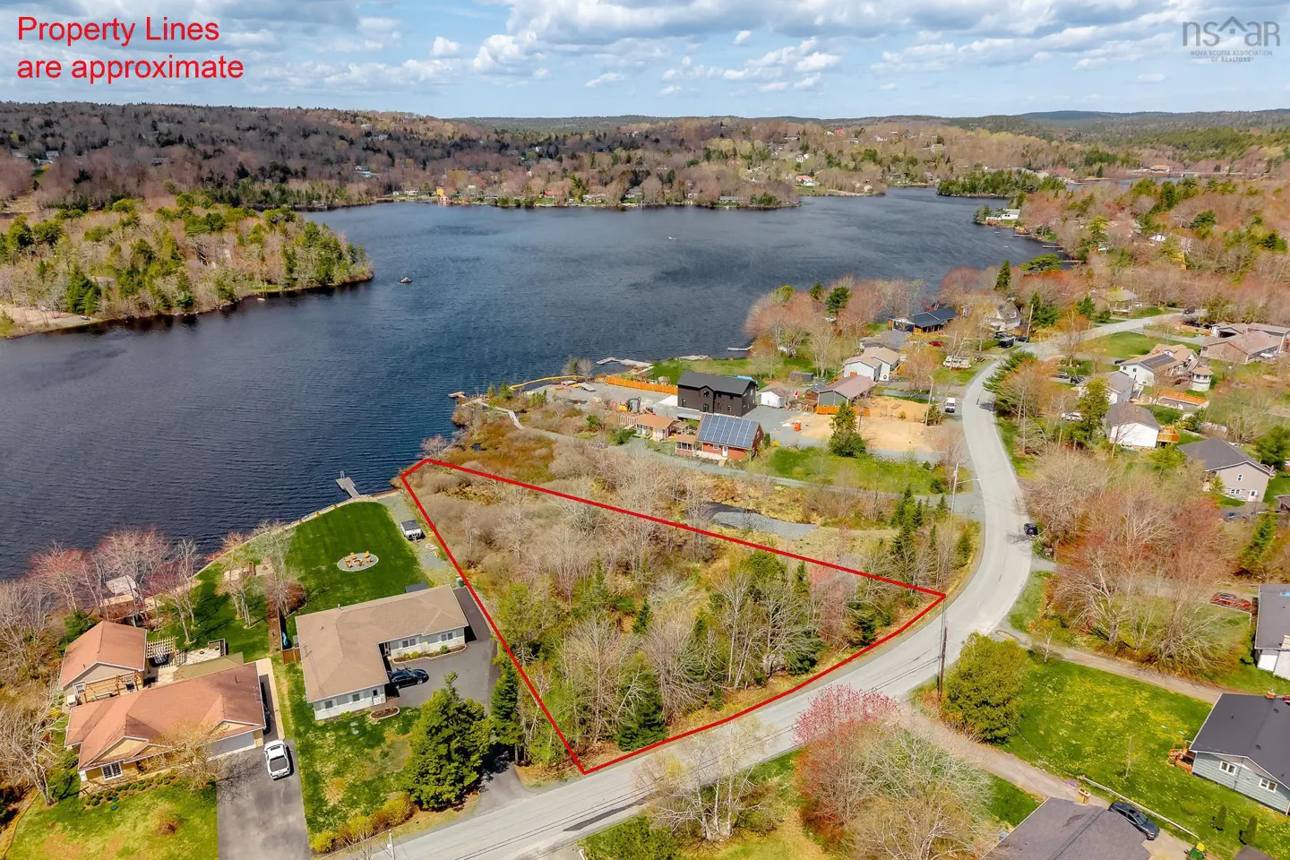 Aerial view of a triangular waterfront lot outlined in red, situated between a road and a lake in a wooded neighborhood.