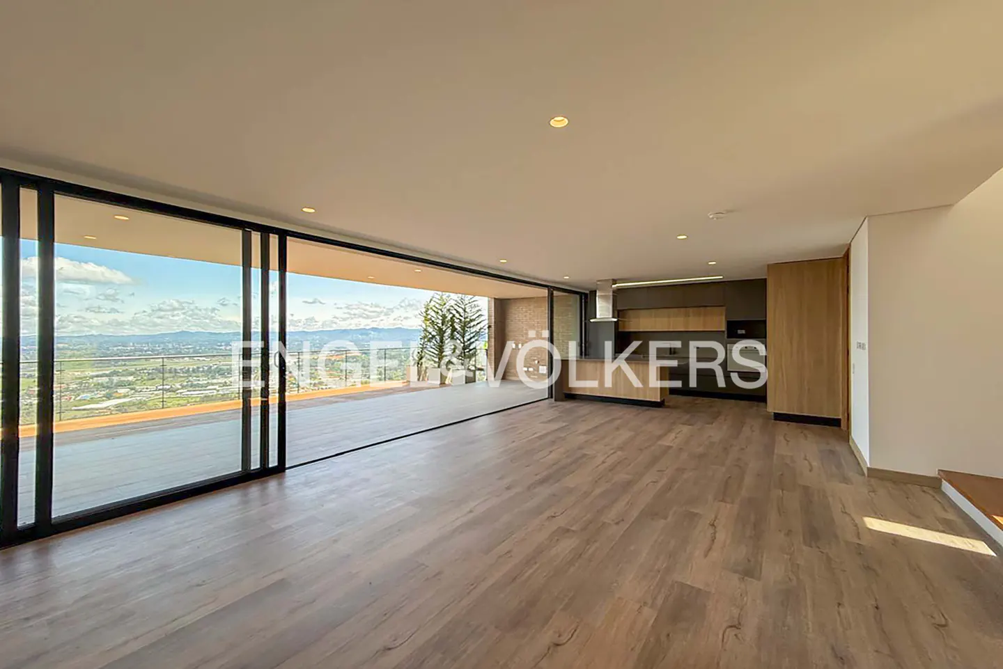 A bright, open-concept living space with wood floors and a large sliding glass door leading to a balcony with a city view.
