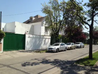A white house with a green gate and three cars parked on the street.