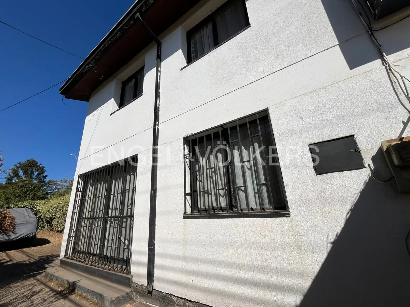 Exterior view of a two-story white house with barred windows and a dark roof against a blue sky.