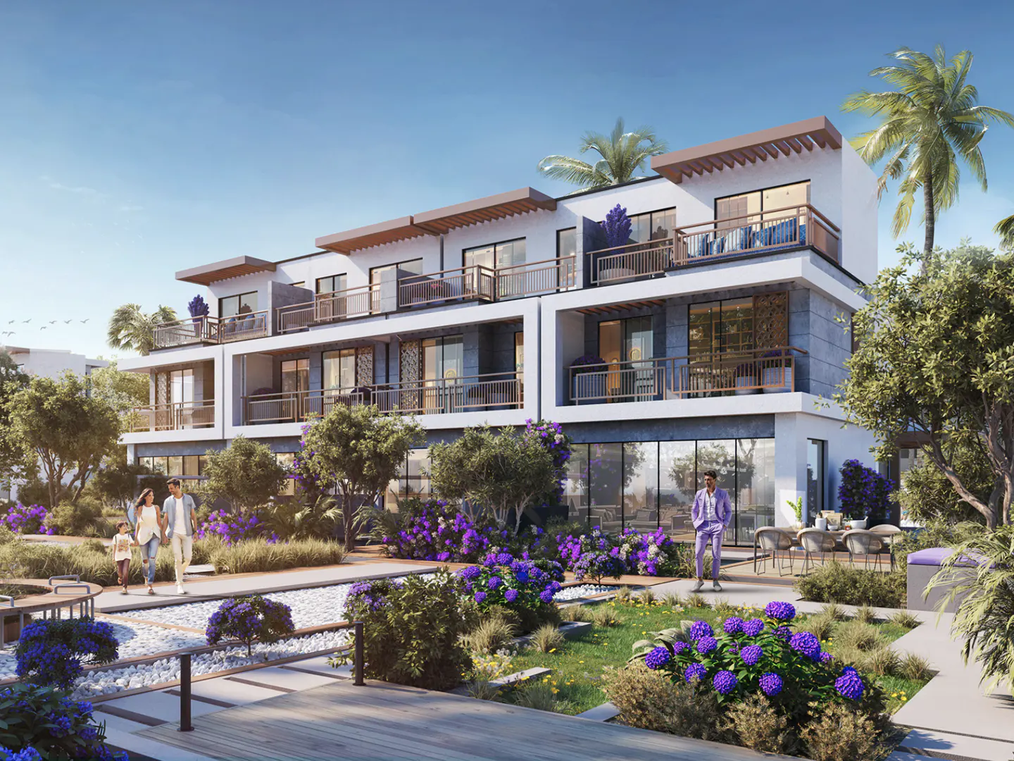 Modern white townhouses with balconies overlook a lush garden with purple flowers and walking paths. Palm trees and blue sky in the background.