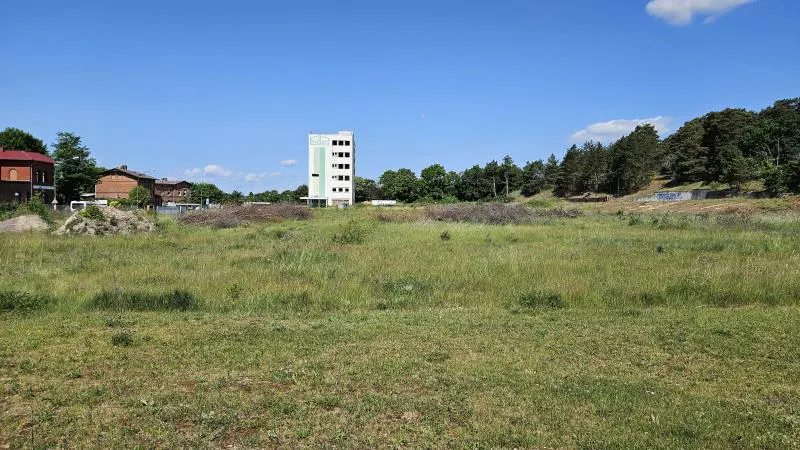 A grassy field with a tall, white building in the background under a blue sky.