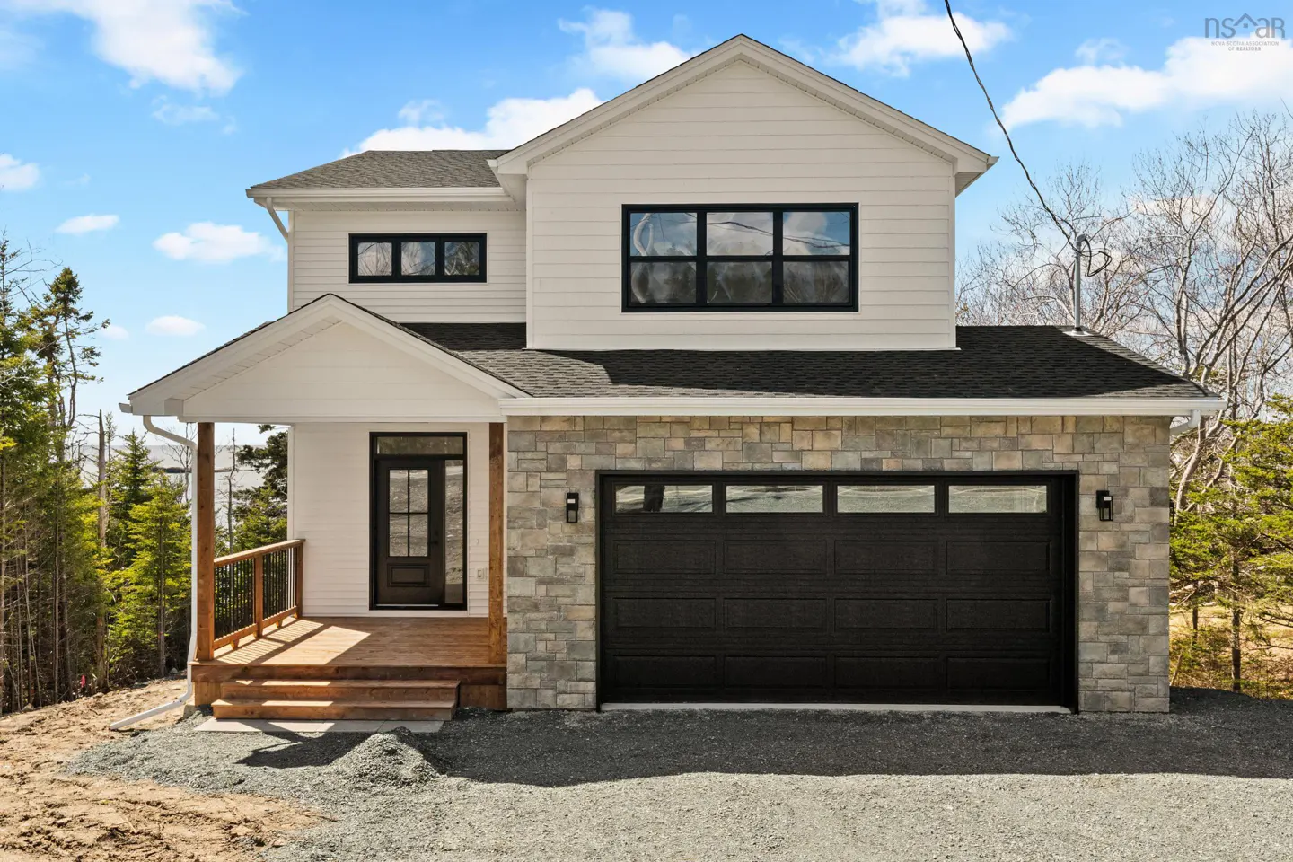 Two-story house with white siding, stone accents, black garage door, and a wooden porch. Blue sky with clouds in the background.