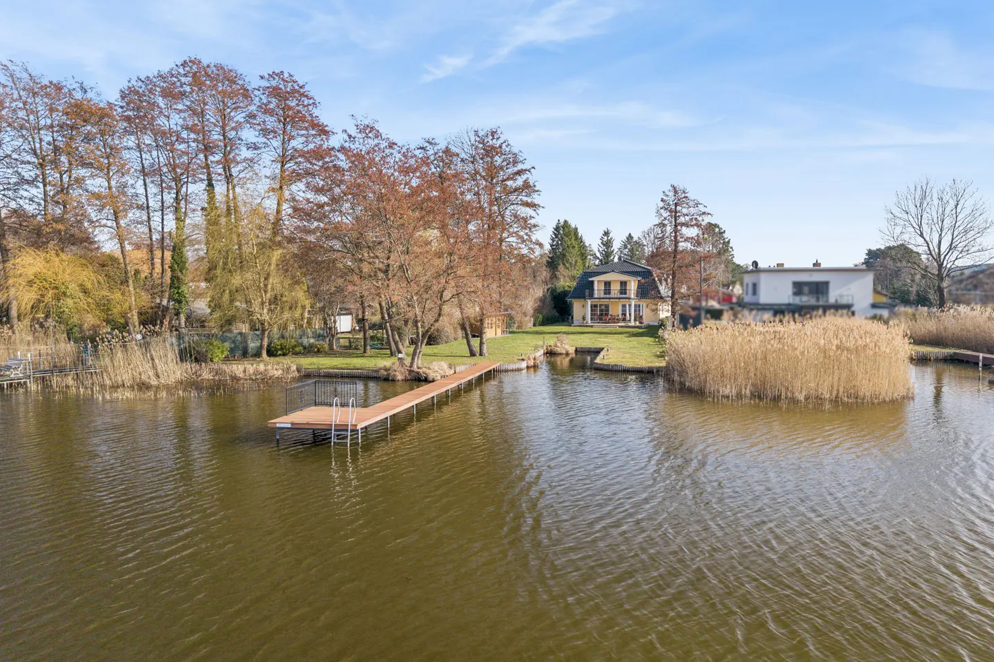 Lakefront property with a wooden dock extending into the water. A yellow house is visible in the background.
