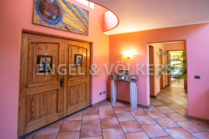 A pink foyer with a terracotta tile floor, wooden double doors, and an abstract painting above. A glass table with framed photos sits against the wall.