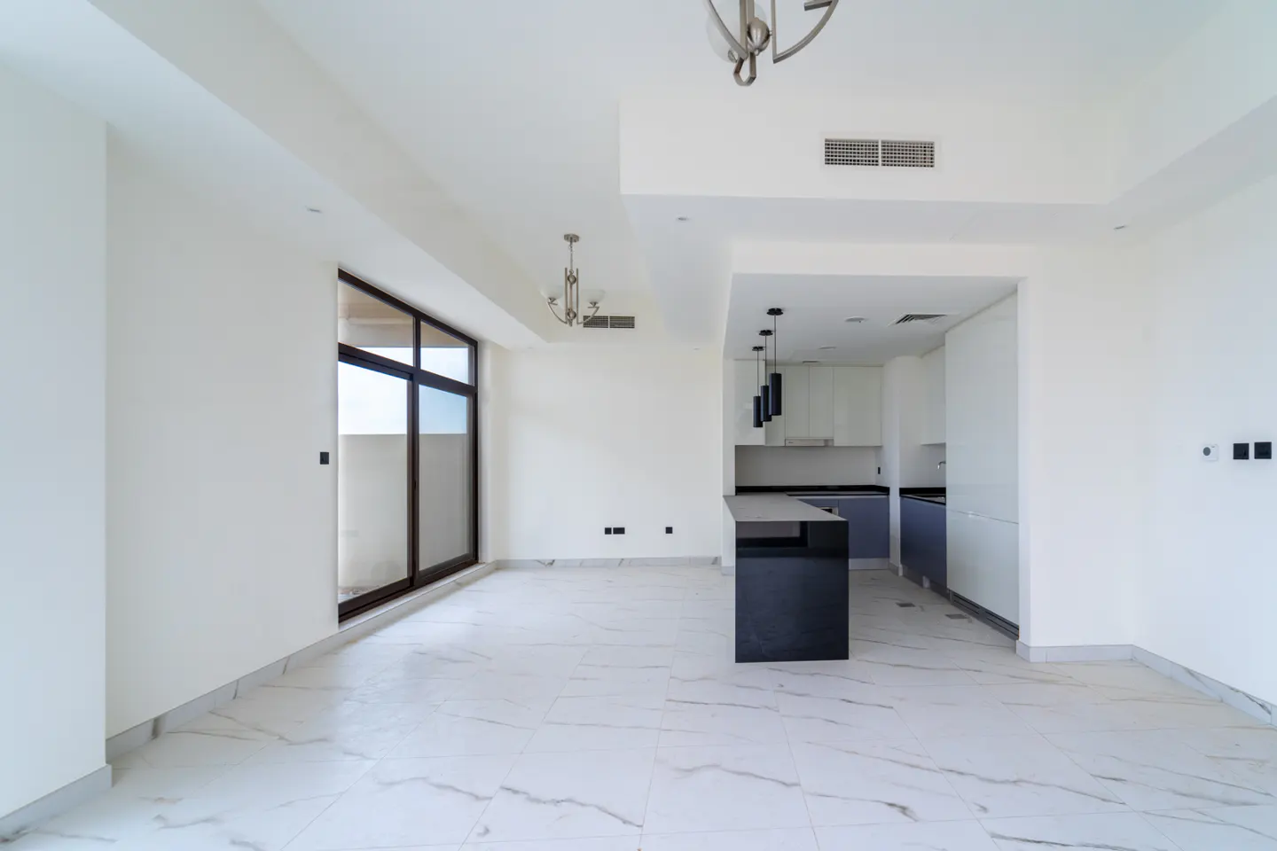 Bright, empty room with white walls, marble floors, and a black kitchen island. A sliding glass door leads to a balcony.