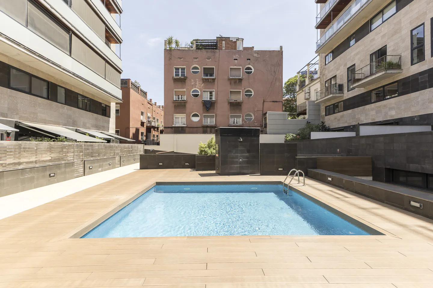 Outdoor pool with light blue water, surrounded by wood-look tile, with buildings in the background.