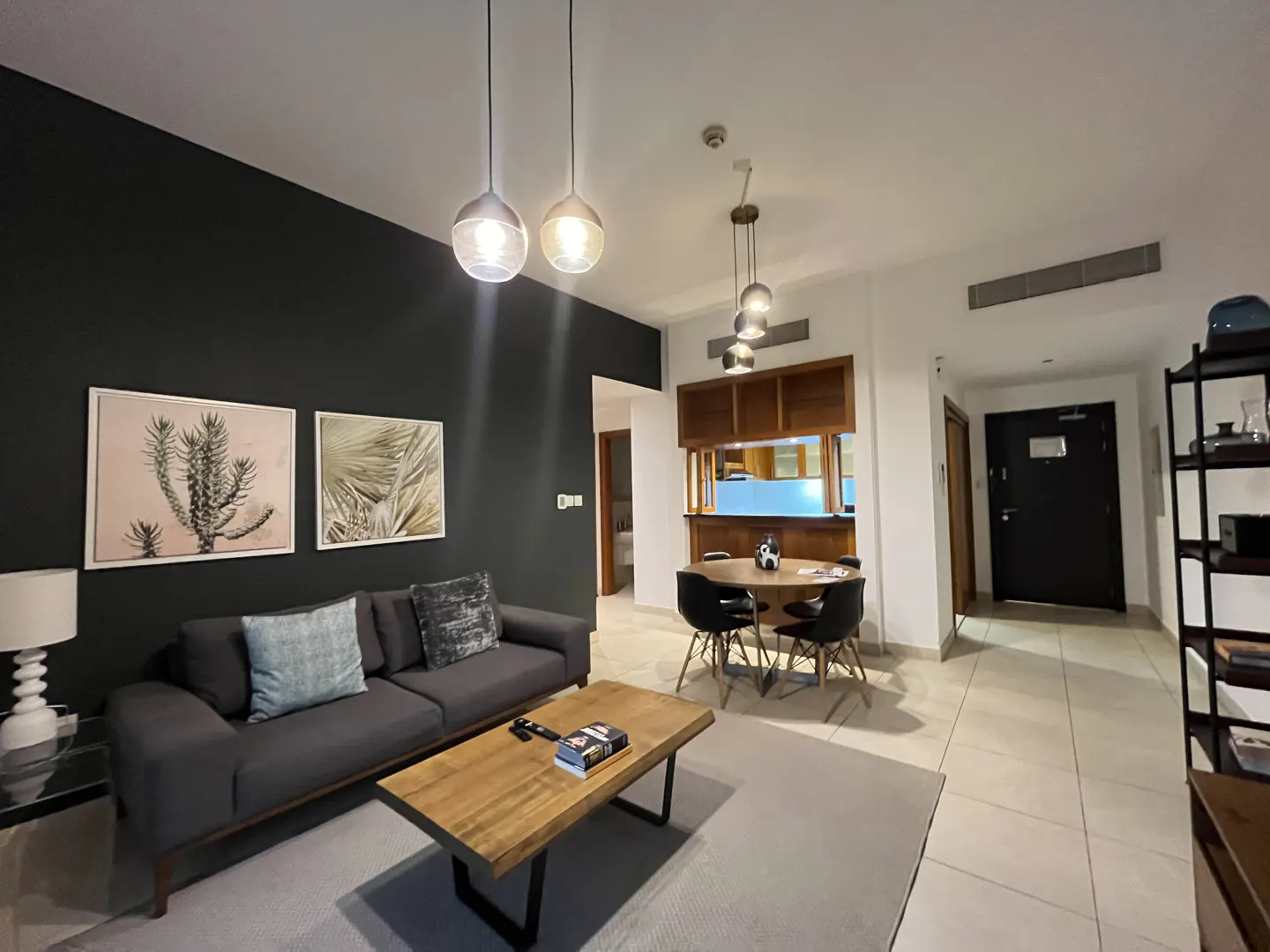 Living room with gray sofa, wood coffee table, and dining area with black chairs. Two botanical prints hang on a dark gray wall.