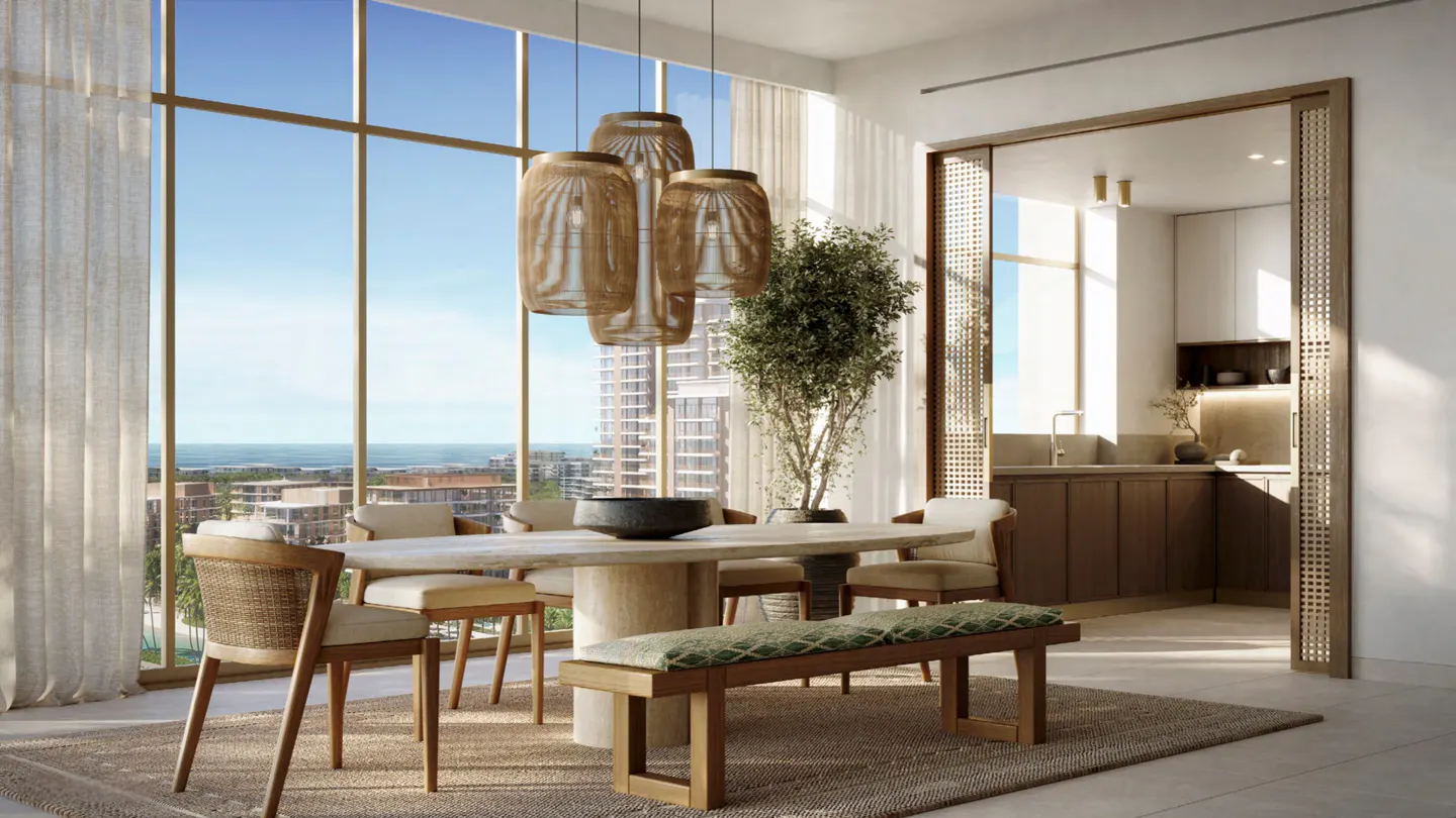 Modern dining room with a stone table, rattan chairs, and a bench, featuring floor-to-ceiling windows and a kitchen view.