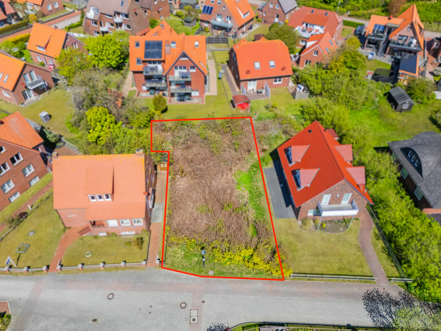 Aerial view of a vacant lot outlined in red, surrounded by houses with orange roofs and green trees.