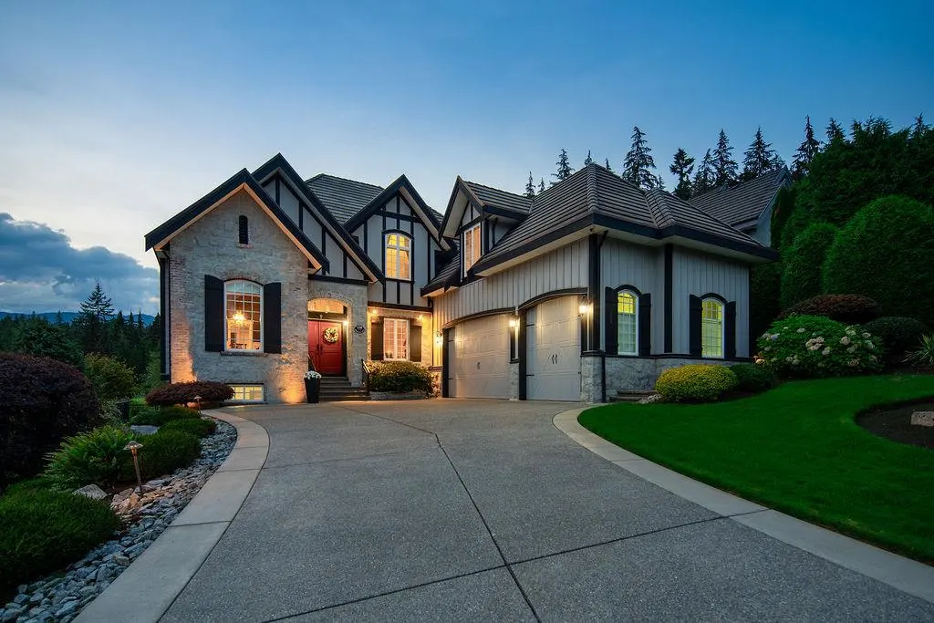 Exterior view of a two-story Tudor-style house with a gray driveway and manicured lawn at dusk.
