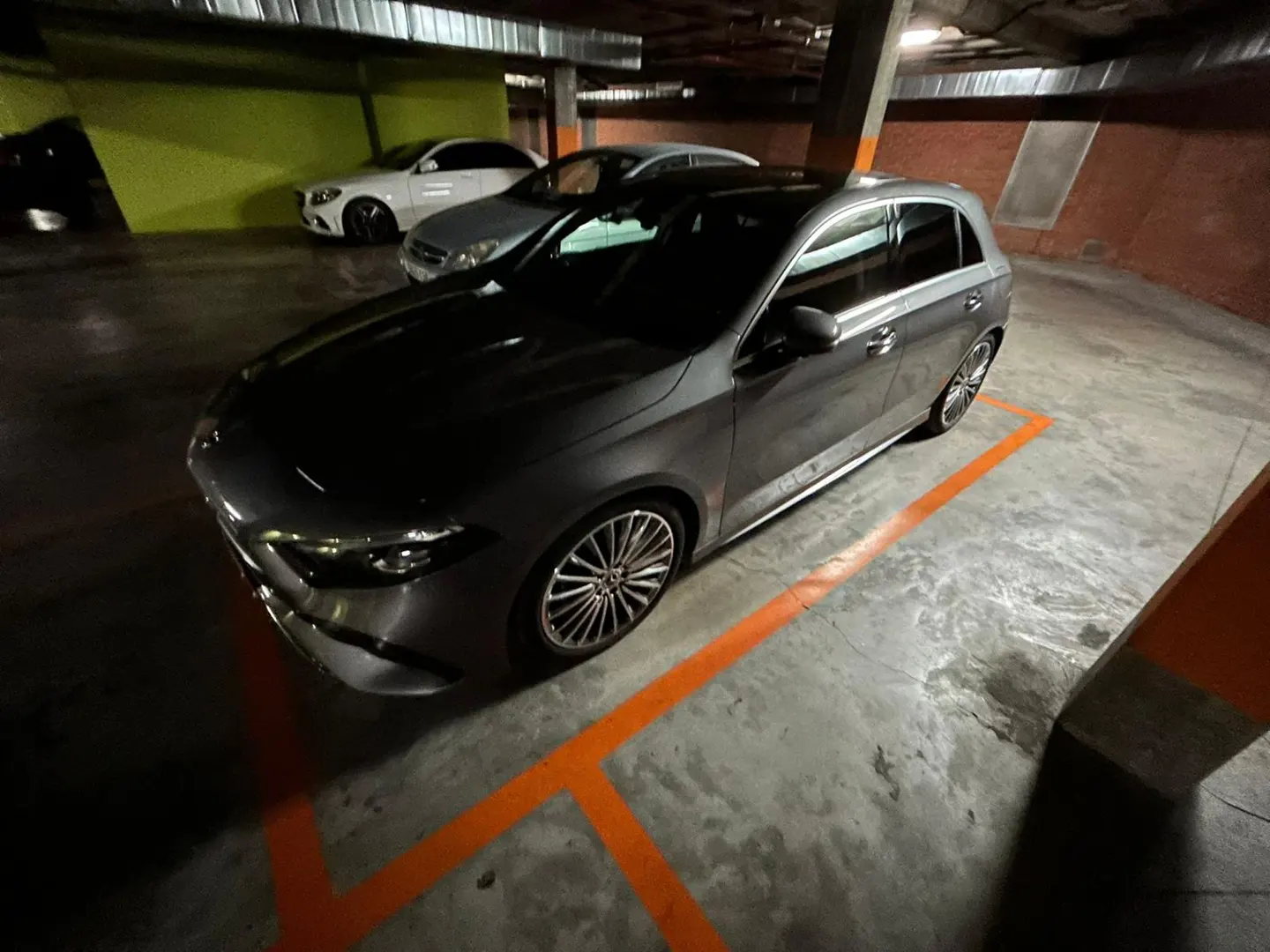 A grey Mercedes-Benz parked in a dimly lit underground garage with orange painted lines on the concrete floor.