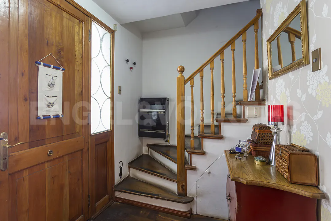 Entryway with a wooden door, staircase, and floral wallpaper. A red cabinet holds decorative items. A mirror hangs on the wall.