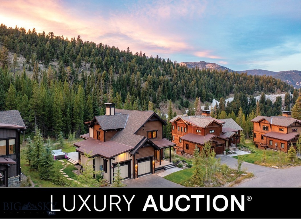 Luxury homes with brown roofs nestled in a green, mountainous landscape under a colorful sunset sky.