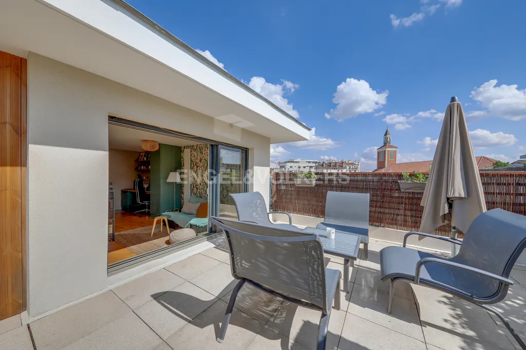 A modern patio with gray chairs, a table, and an open sliding door to an office space, under a blue sky.