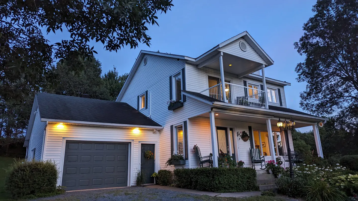Two-story white house with a gray garage door and a porch with rocking chairs at dusk.