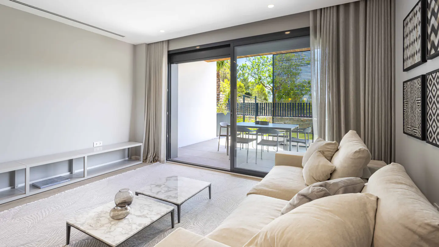 Living room with a beige sofa, marble coffee tables, and sliding glass doors to a patio with outdoor seating.