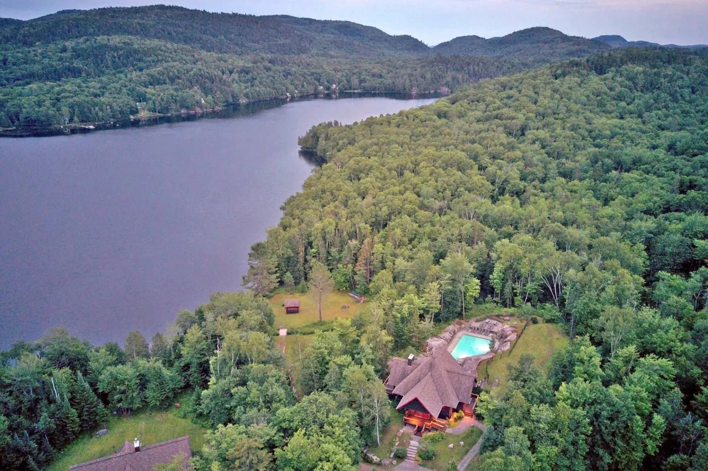 Aerial view of a lake house with a pool surrounded by green trees and a lake.